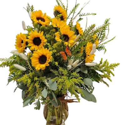 Sunflowers in a vase with seasonal greens and dried bunny tails.